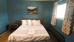 Een opgemaakt bed met hoofdeinde, een klein nachtkastje en een schilderij aan de muur.