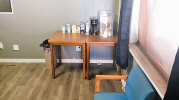 Une petite pièce avec une table en bois, une chaise bleue et une fenêtre avec des rideaux.