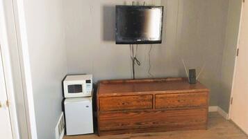 Une chambre avec un téléviseur fixé au mur, un four à micro-ondes et une commode en bois.