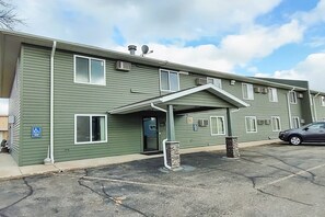 A multi-story building with a covered entrance, air conditioning units, and a parking lot. - Cozy King Bed | Staples (Staples)