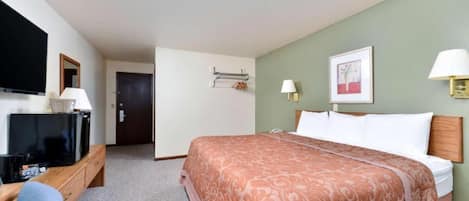 A hotel room with a bed, a TV, a desk, and a door.