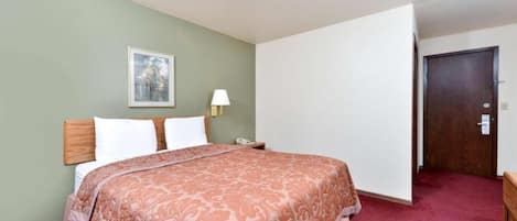 A hotel room with a bed, a nightstand, a lamp, a door, and a framed picture on the wall.