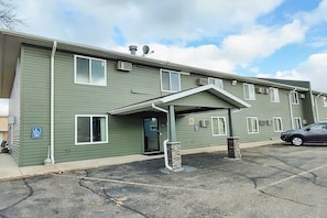 A multi-story building with a covered entrance, air conditioning units, and a parking lot. - Staples | Relaxing Queen Bed (Staples)