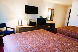Une chambre d’hôtel avec deux lits, un bureau avec une lampe, une télévision et un miroir.