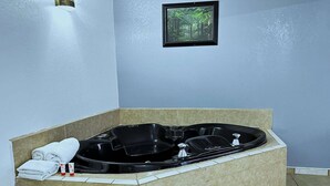 A bathroom with a large black bathtub, a framed picture on the wall, and a towel rack with towels.