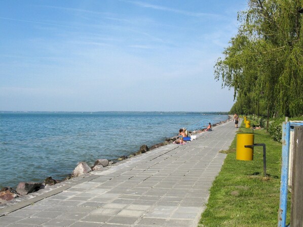 Ein gepflasterter Weg entlang des Wassers, an dem sich Menschen entspannen und spazieren gehen.