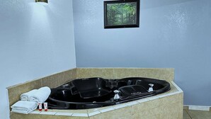 A spa room with a black jacuzzi tub, towels, and a framed picture on the wall.