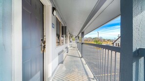 Ein überdachter Balkon mit einem Metallgeländer, einer Tür und freiem Blick auf die Straße und die dahinterliegenden Gebäude.