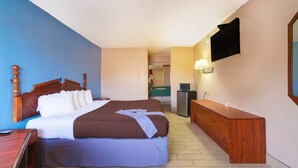 Ein Hotelzimmer mit einem großen Bett, einem hölzernen Kopfteil, einem Nachttisch, einem an der Wand befestigten Fernseher und einem kleinen Schreibtisch mit einer Lampe.