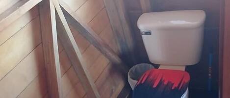 Une salle de bain aux murs lambrissés, avec des toilettes, un tapis et une fenêtre.