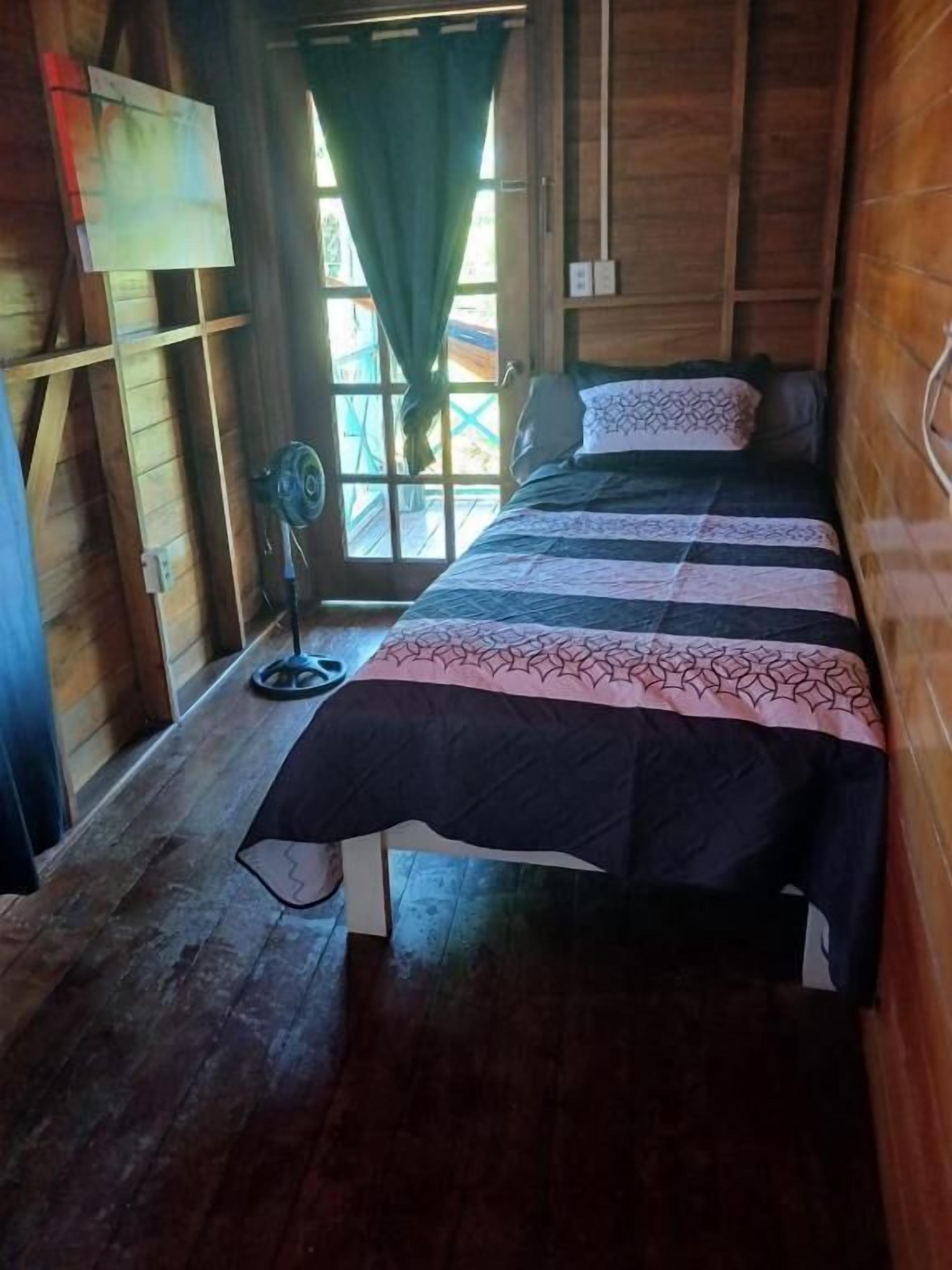 A wooden room with a bed, a fan, and a window with curtains.
