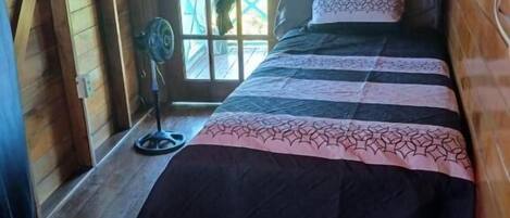 A wooden room with a bed, a fan, and a window with curtains.