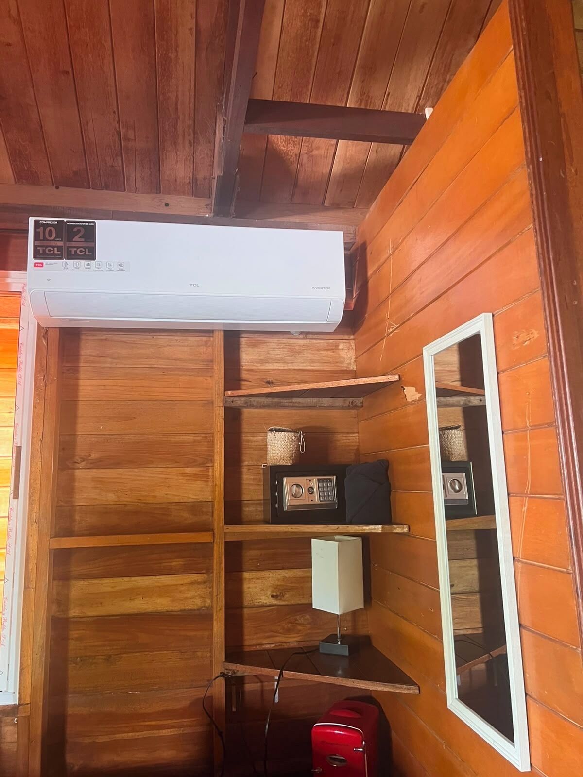 A wooden interior with a white air conditioner, a radio, a lamp, and a red suitcase.