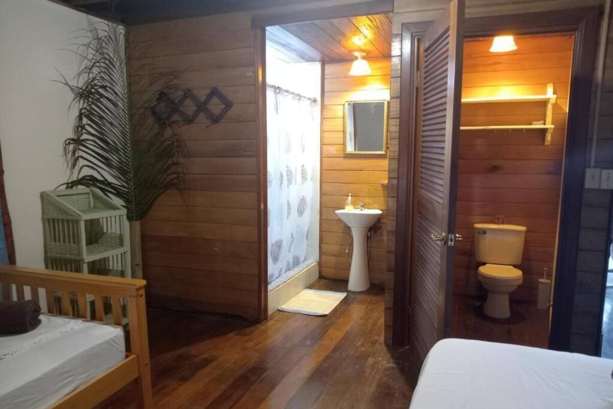 A wooden interior with a bed, a small table, a sink, and a toilet.