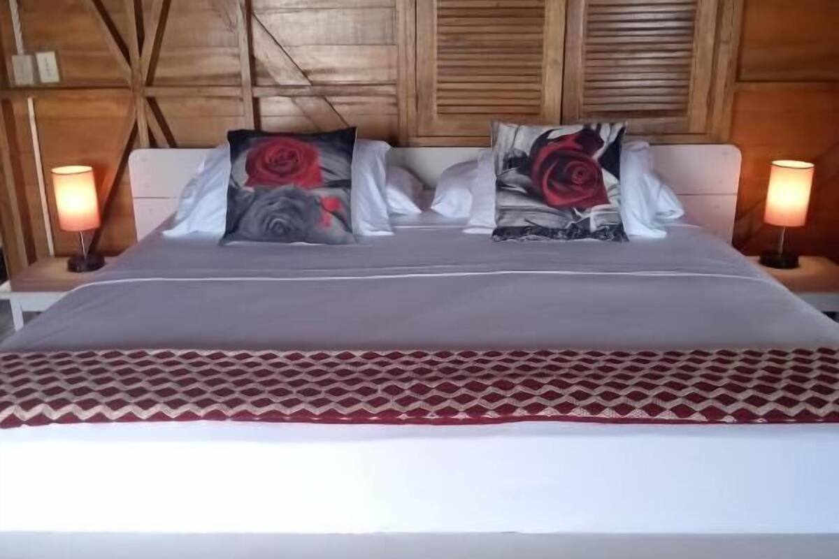 A bed with a patterned bedspread, a painting of a tree on the wall, and two bedside lamps.