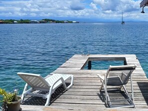 A wooden pier with two white lounge chairs and a small table, overlooking a calm sea with a sailboat in the distance. - VILLA BAHIA DEL SOL (Bocas del Toro)