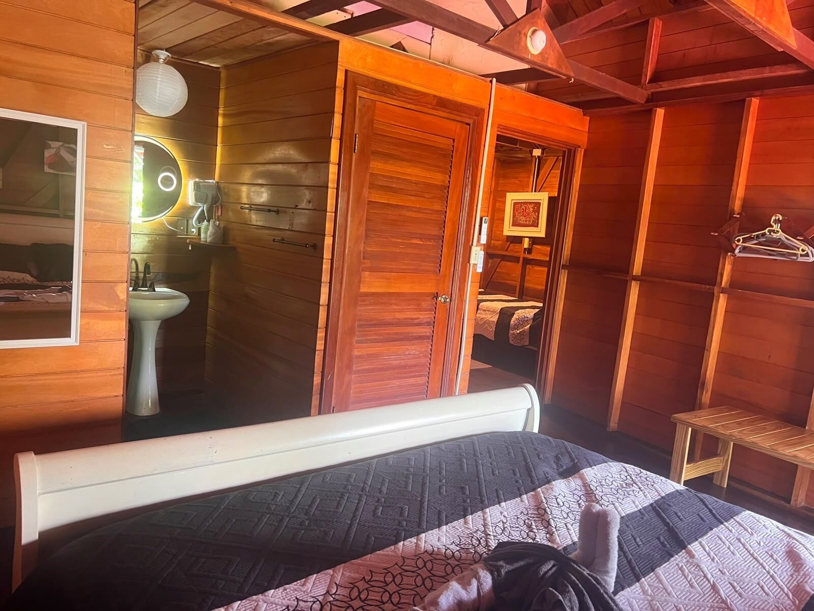 A wooden room with a bed, a sink, and a mirror.