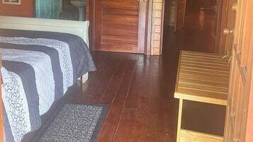 A wooden room with a bed, a small table, a door, and a mirror.
