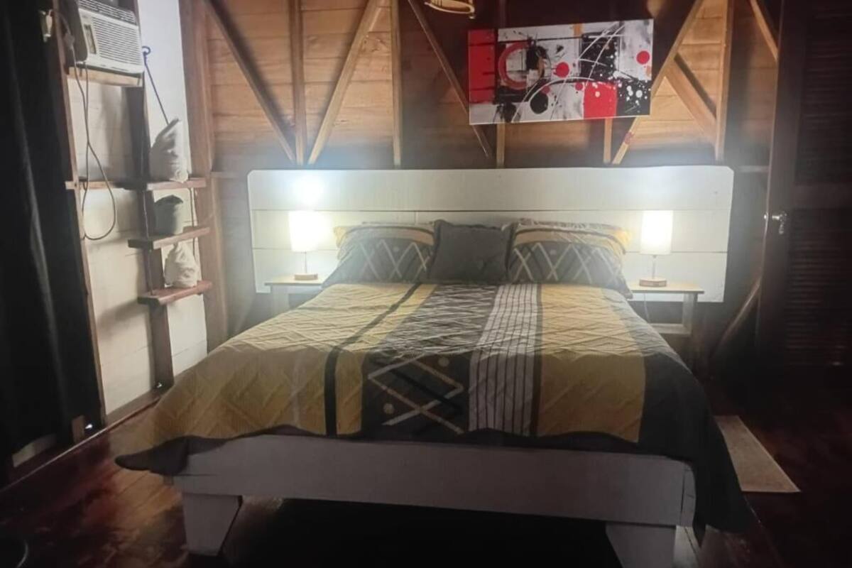 A room with a bed, a wall-mounted air conditioner, a shelf with items, and a painting on the wall.