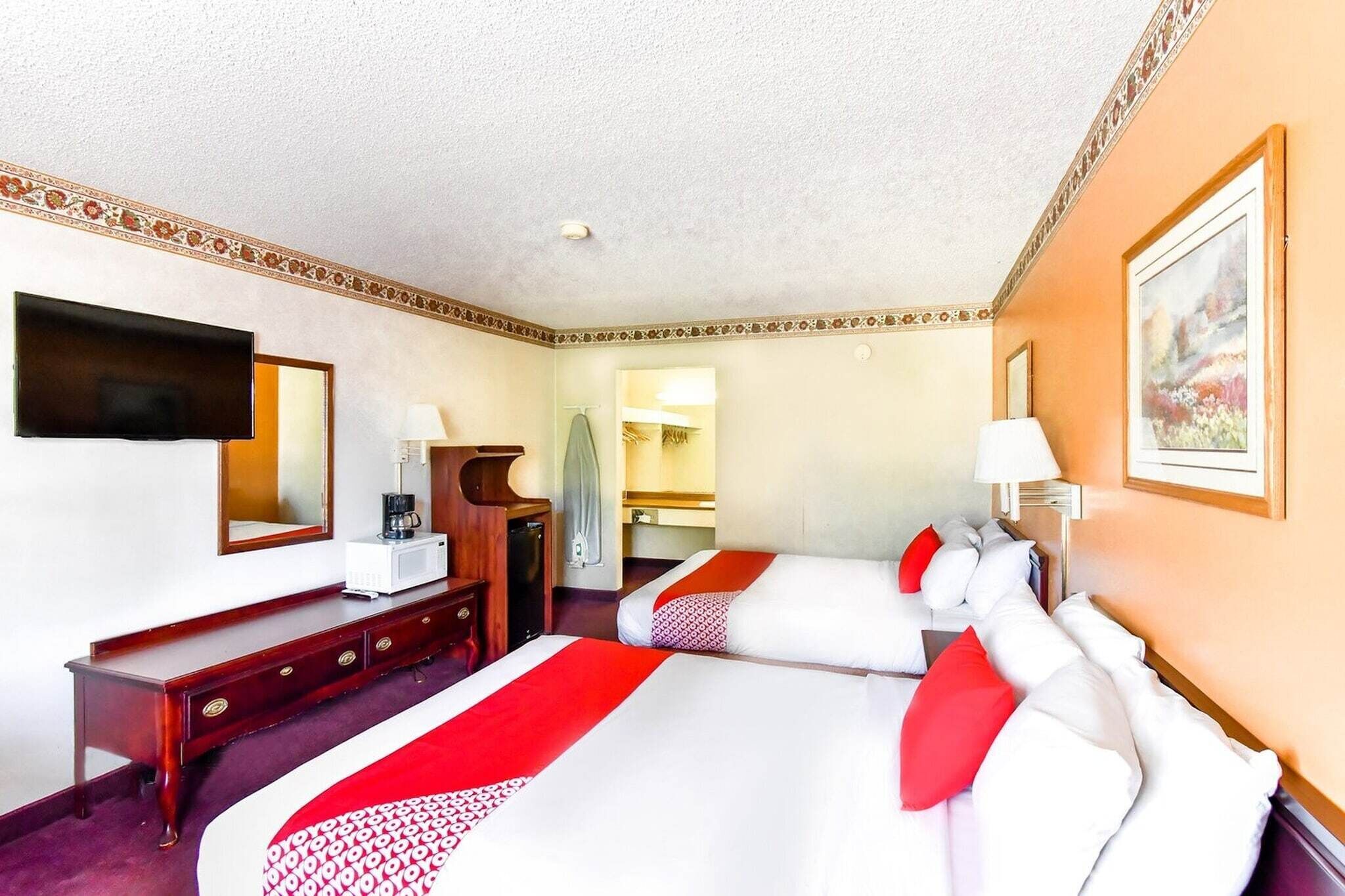 Ein Hotelzimmer mit zwei Betten, einem Fernseher, einem Schreibtisch und einem Spiegel.