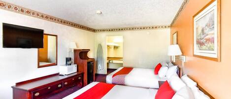 Ein Hotelzimmer mit zwei Betten, einem Fernseher, einem Schreibtisch und einem Spiegel.
