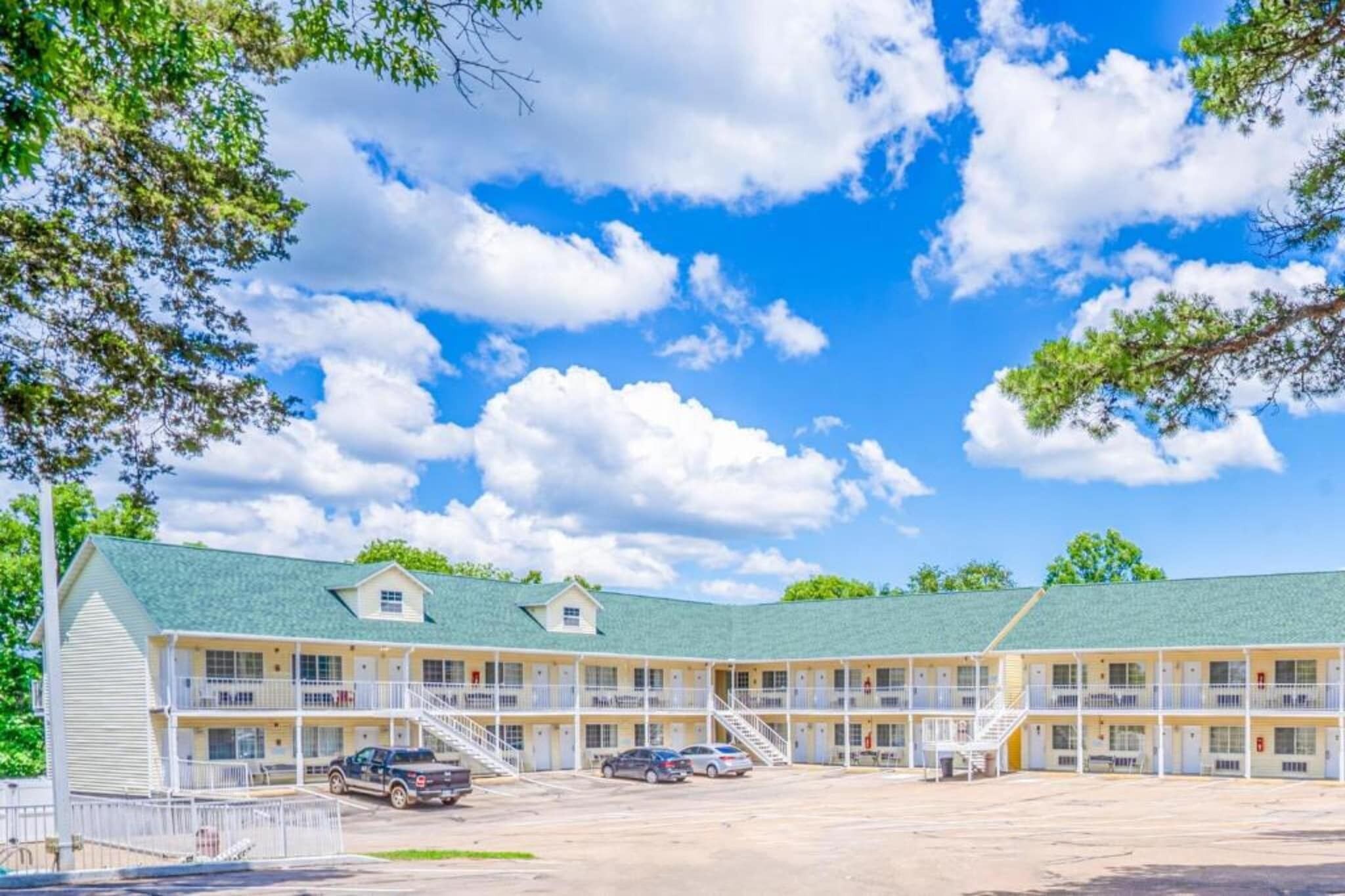 A motel with a green roof, multiple balconies, and a parking lot.
