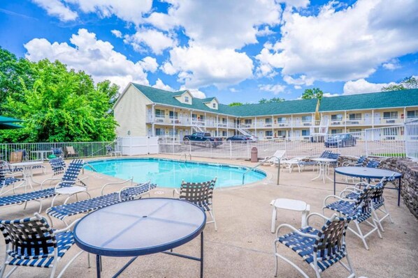 A hotel with a swimming pool, outdoor seating, and a multi-story building.