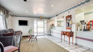 A hotel lobby with a sofa, a small table, a coffee machine, and a TV on the wall.