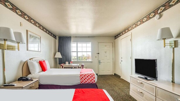 A hotel room with two beds, a television, a desk, and a window.