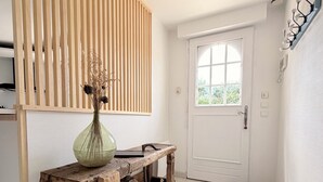 Un pasillo con un banco de madera, un jarrón con flores secas, una puerta blanca y una pared con textura.