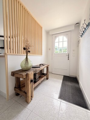 Ein Flur mit einer hölzernen Bank, einer Vase mit Trockenblumen, einer weißen Tür und einer strukturierten Wand.