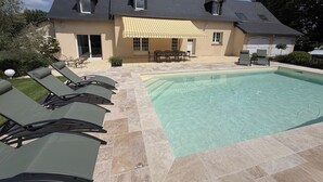 Una casa con piscina, mobiliario de exterior y un porche cubierto.