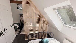 Un dormitorio con techo inclinado, una cama con colcha blanca estampada, cabecero de madera, una ventana con vistas y una escalera con barandilla de madera.