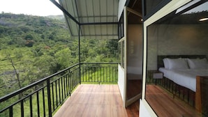 A balcony with a view of a lush green landscape, a wooden floor, and a bed with white bedding.