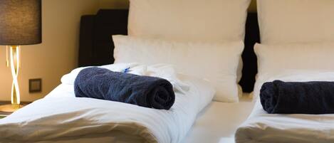 Habitación de hotel con dos camas, ropa de cama blanca y una lámpara en una mesita de noche.
