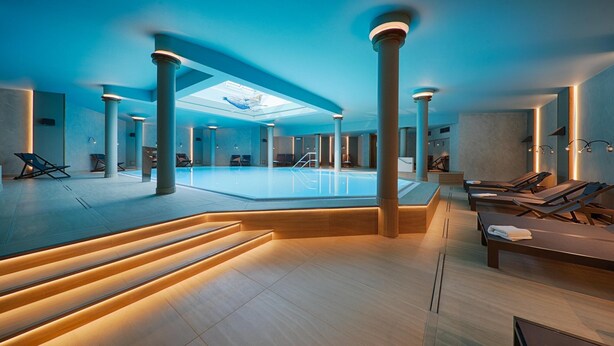 Tilava sisäuima-allasalue, jossa on pääallas, syvennetty oleskelualue ja kattovalokuvio.
