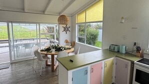 Eine moderne Küche mit einer zentralen Kochinsel, einem Essbereich mit Tisch und Stühlen sowie großen Fenstern mit Blick ins Grüne.