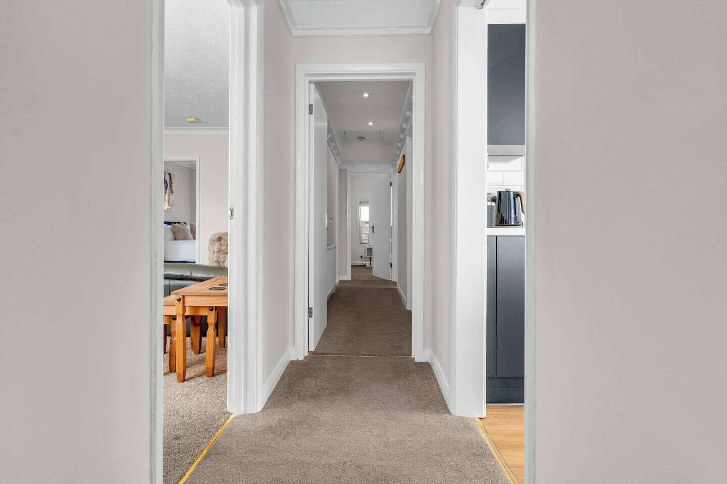 A hallway leading to a kitchen and dining area with a carpeted floor and white walls.