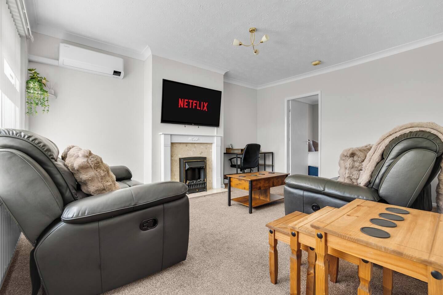 Moderni olohuone, jossa on takka, nahkasohvat, puinen sohvapöytä ja litteänäyttöinen televisio, jonka näytöllä näkyy teksti ”NETFLIX”.