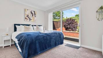 A bedroom with a bed, a nightstand, a window, and a door leading to an outdoor area.