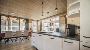A modern kitchen with wooden cabinets, a black coffee machine, and a large window overlooking a mountainous landscape. - Stylish Holiday Home Dein Bichelbach (Bichlbach)
