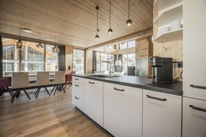 Una cocina moderna con armarios de madera, una cafetera negra y un ventanal con vistas a un paisaje montañoso.