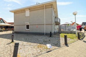 Ein kleines, eingeschossiges Gebäude mit Backsteinfassade, einem kleinen Fenster und einer Tür. Vor dem Gebäude verläuft ein Maschendrahtzaun, und ein Parkschild ist auf dem Boden sichtbar.