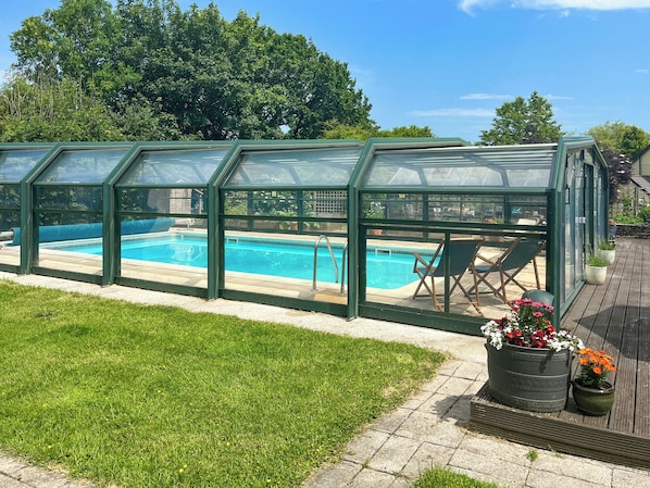A swimming pool with a glass enclosure, surrounded by a grassy area and potted plants.