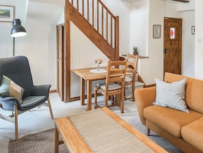 A living room with a wooden dining table, chairs, a sofa, a bench, and a staircase.