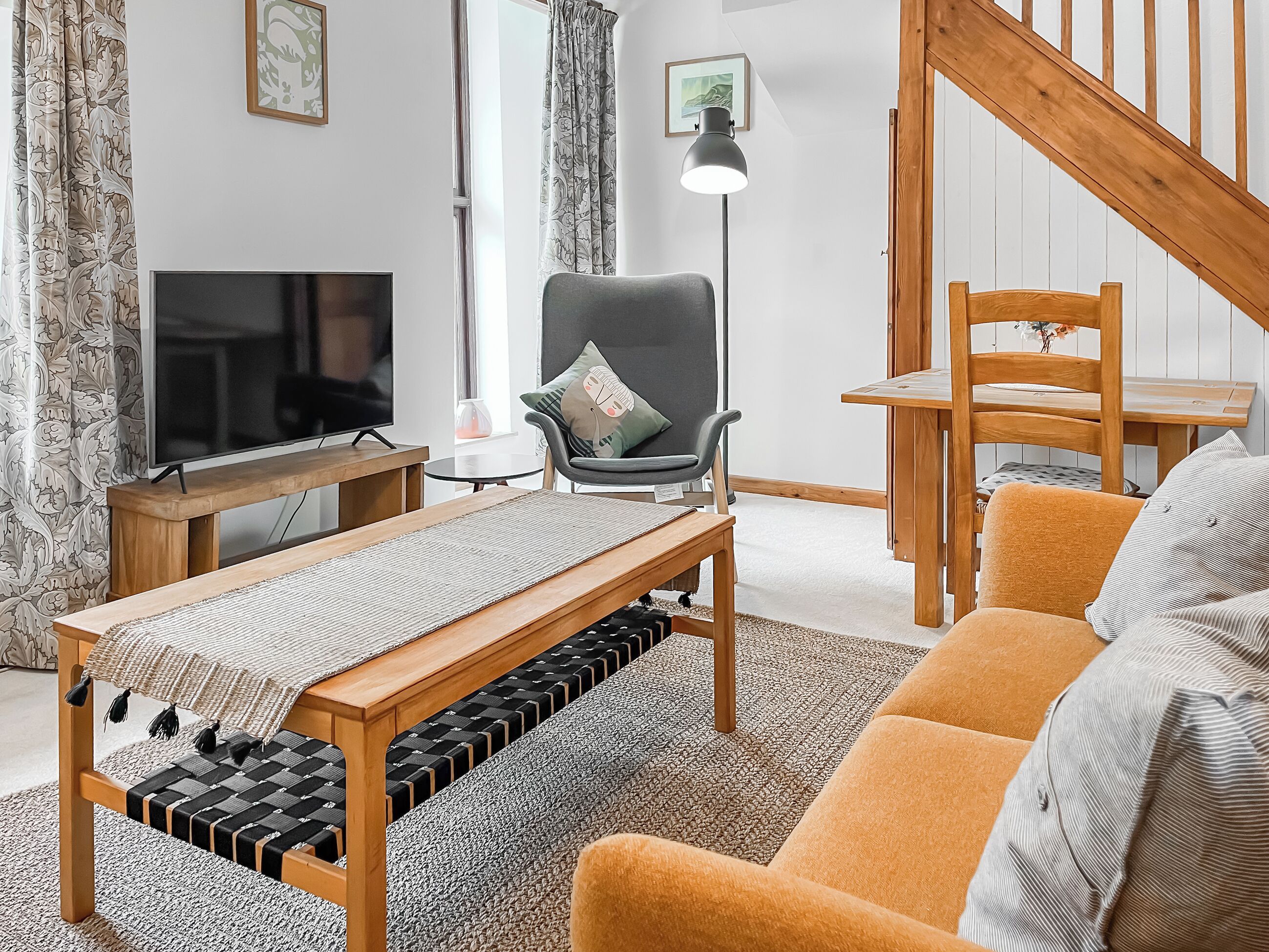 A living room with a TV, a chair, a sofa, a table, and a staircase.