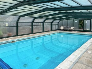 An indoor swimming pool with a glass ceiling, clear pool water, and two lounge chairs.