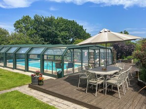 A glass-enclosed pool with a patio area, outdoor furniture, and a large umbrella. - Bridge Cottage - UKC9516 (Sheepwash)