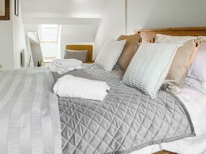 A neatly made bed with a quilted grey duvet, a white throw blanket, and several pillows in shades of white and beige.