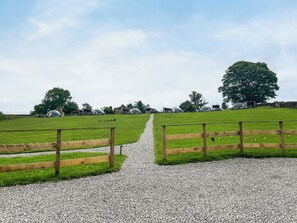 Ein Kiesweg führt zu einem grünen Feld mit Holzzaunen und transparenten Gebäuden.